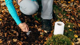 A hiker digs a hole to poop in the woods
