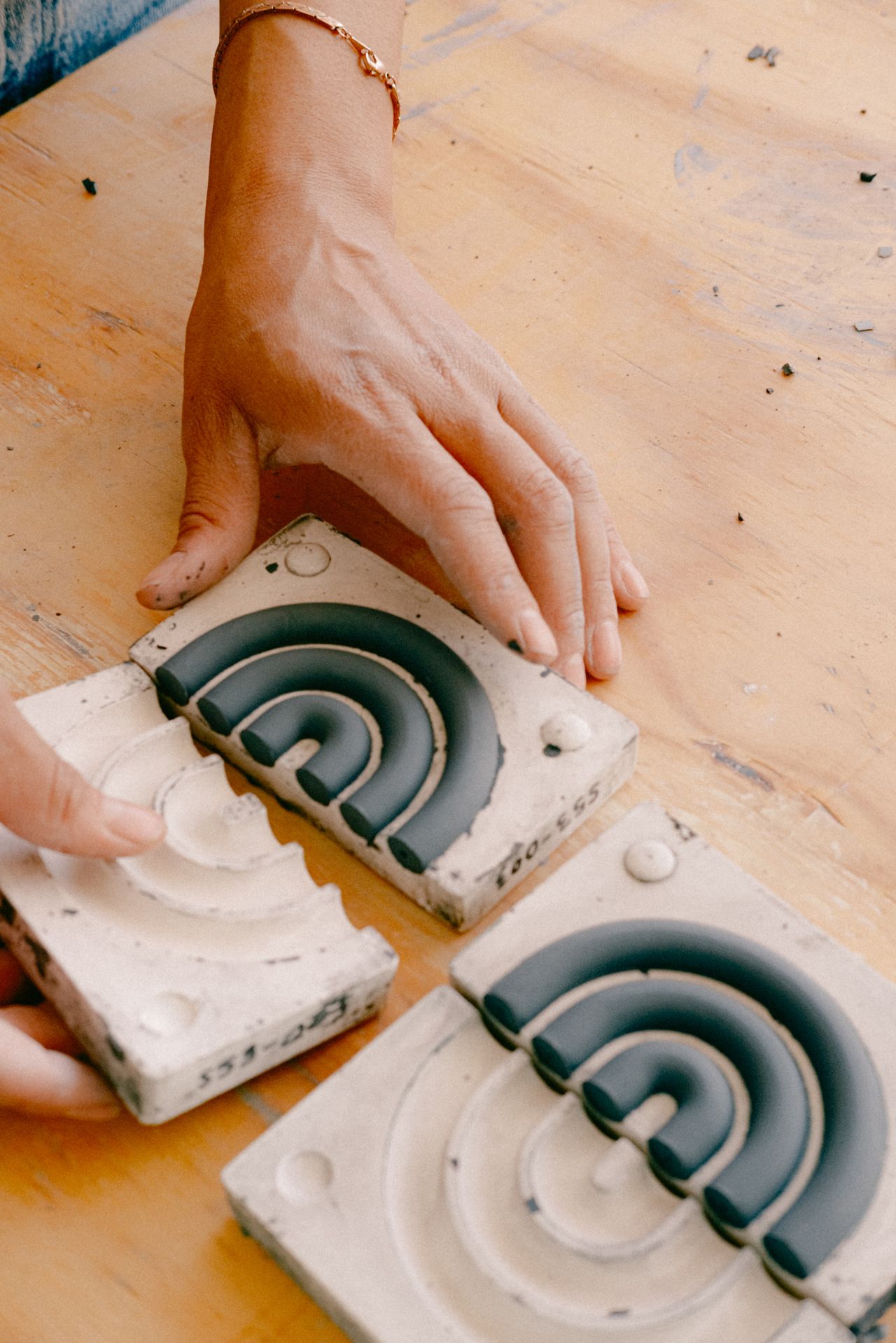 Close-up image of a wooden table. A person's hands are putting together a clay mold for a wavy handle.