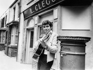 Actor Bill Kenwright who plays Gordon Clegg in the television soap opera Cornation Street, poses in the famous street with his guitar shortly before the release of his new record which he will sing on the programme, 23rd July 1968.