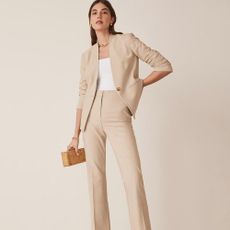A person wearing a tan blazer and trousers holding a handbag