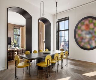 Trevor Noah's Penthouse – dining room with double height archways, large window with city views, and bright yellow chairs