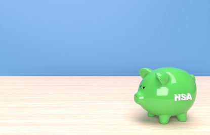 HSA written on green piggy bank on table against blue background