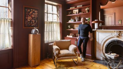 jason saft interior designer in color drenched room with fireplace, armchair, plinth and vase, in front of bookshelf