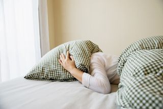 Pelvic floor dysfunction: Young Woman Covering Pillow Lying On Bed Against Wall At Home