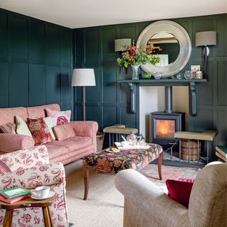 snug with dark panelled walls, pink sofa and light ceiling with lamps and wood-burner