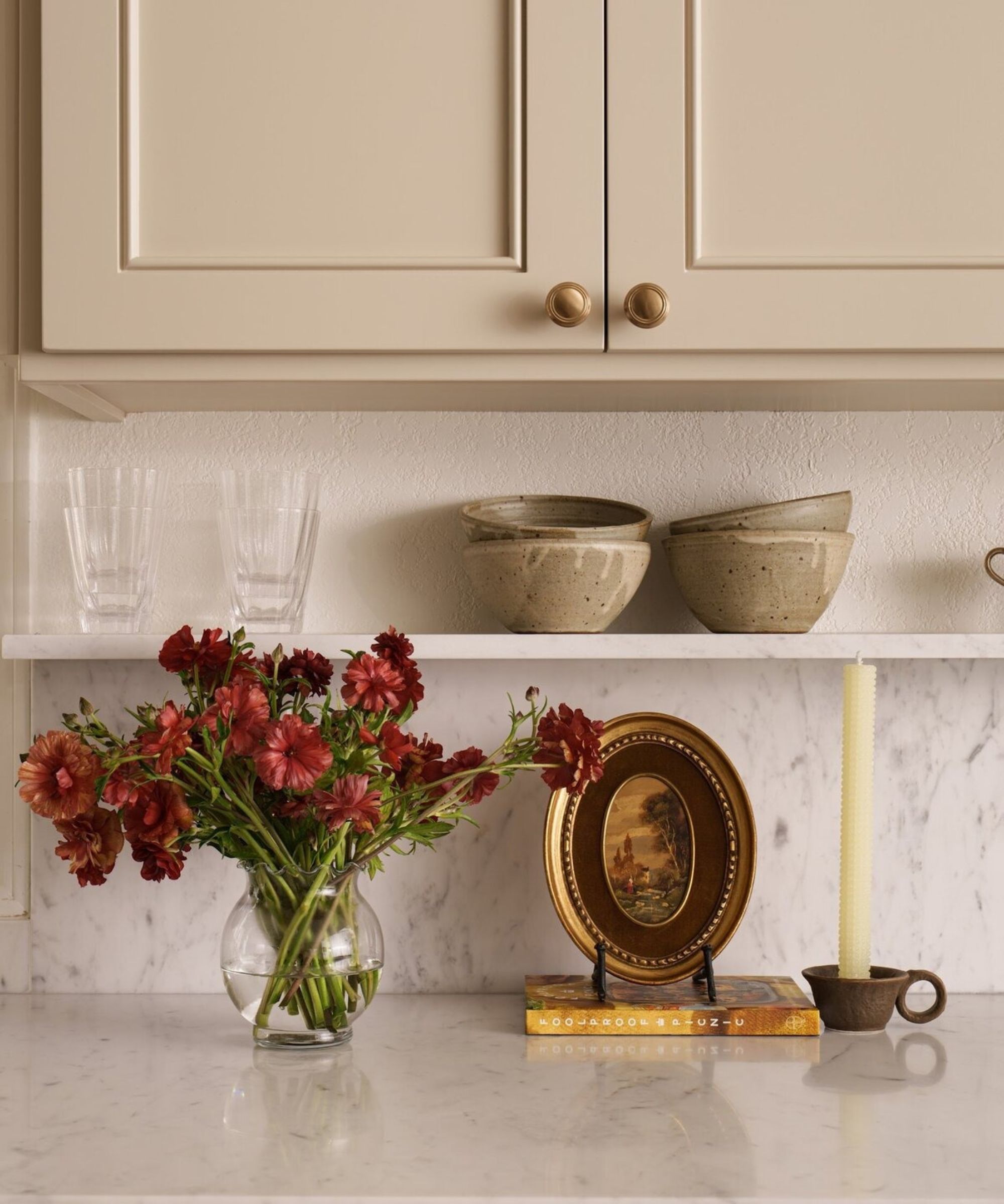 a kitchen countertop moment with a vase of flowers, a round picture frame, a book, and a candle