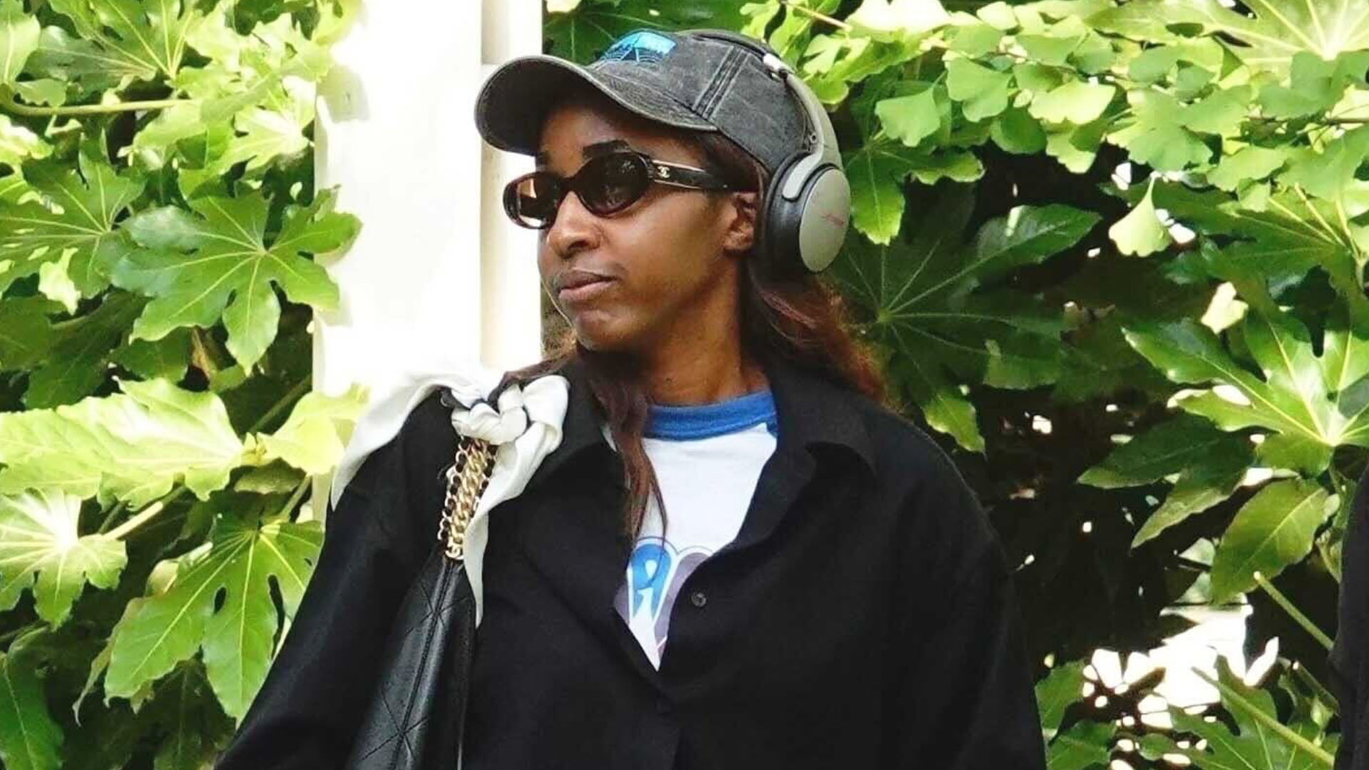 Ayo Edebiri wearing a gray baseball cap, white t-shirt, black button down, black track pants, and white sneakers
