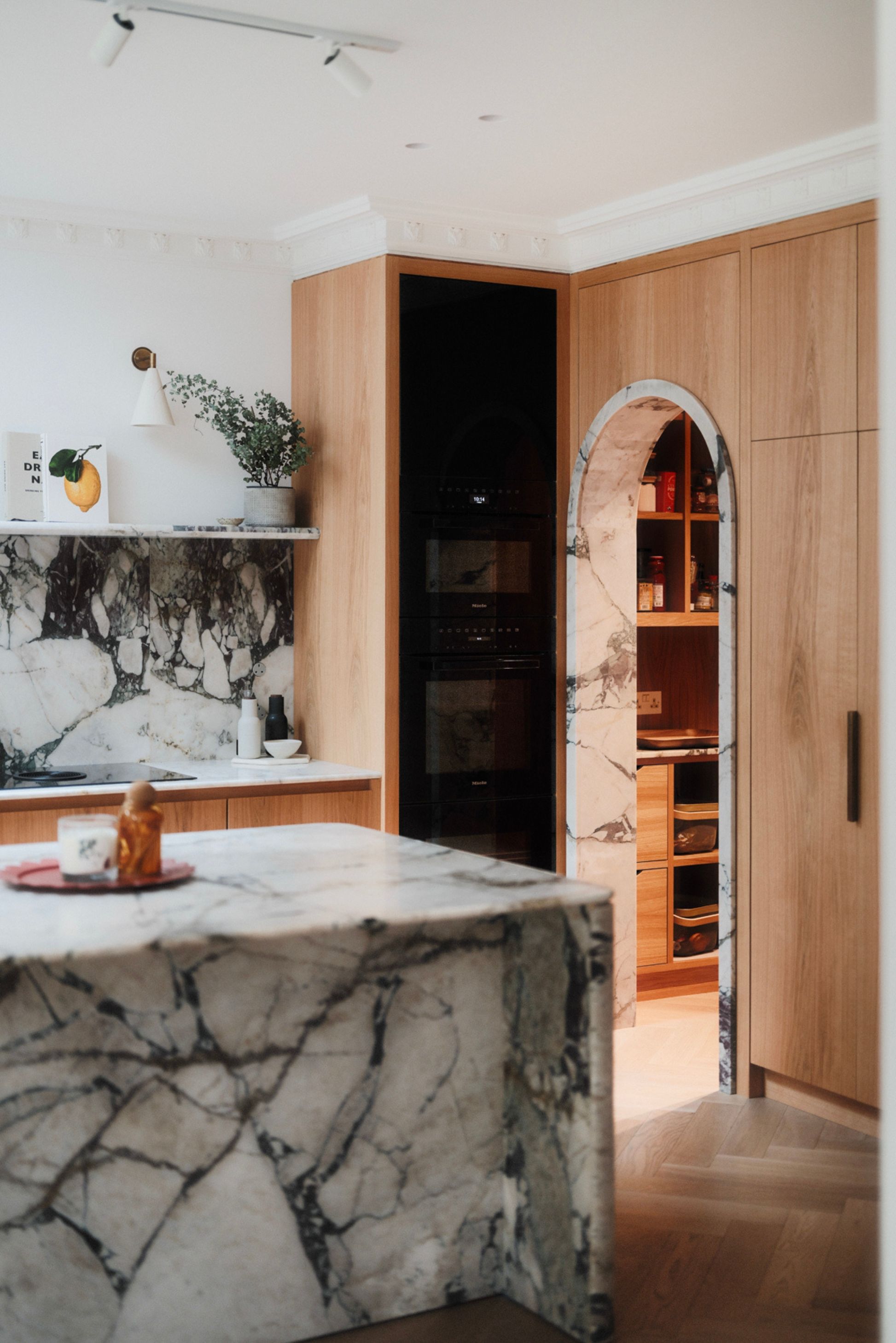 a wood kitchen with a marble island and backsplash with an arched doorway 