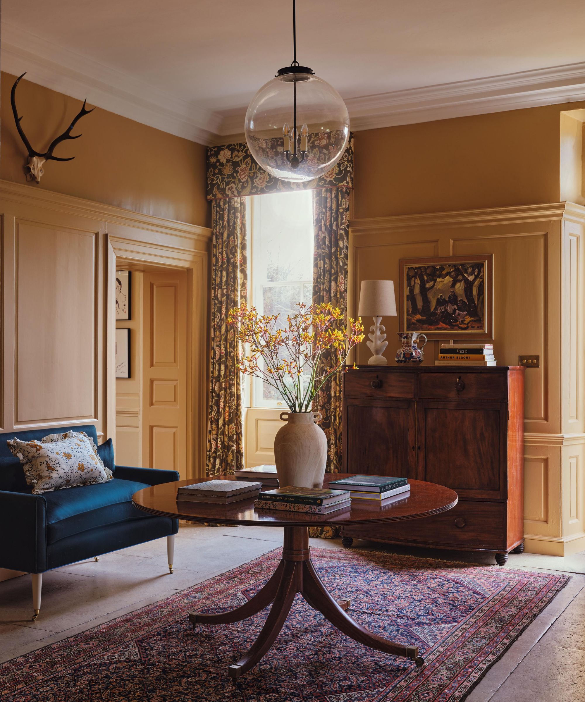 the entryway to a grand English country home with yellow paneled walls, antique furniture and a large vintage rug