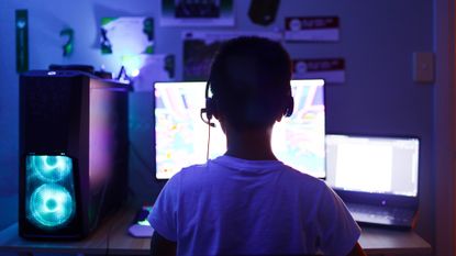Silhouette of a young boy wearing a headset, illuminated by the glow of his computer screens