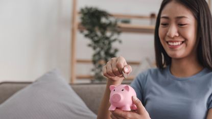 A young woman puts money into a piggy bank.