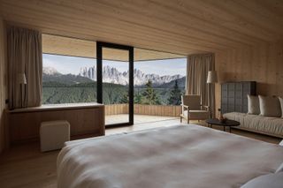 A wood-drenched hotel room stands out for its floor-to-ceiling windows letting in panoramic alpine views and linearly precious furnishings.