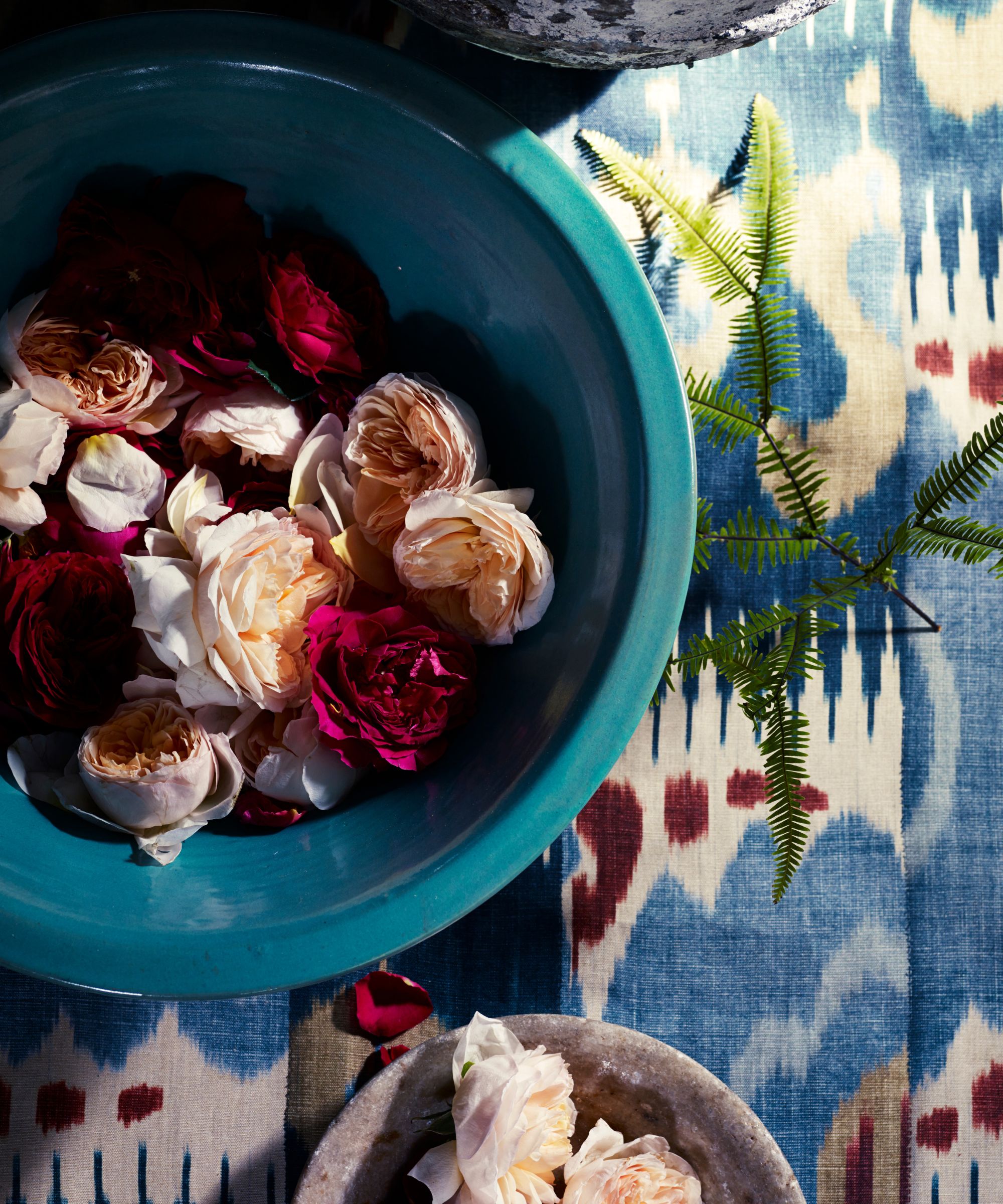 dark and light pink peonies and roses in a turquoise bowl on a printed tablecloth in blue, red and white