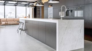 Contemporary apartment with large marble worktop and island with a bank of dark kitchen units in backgound.