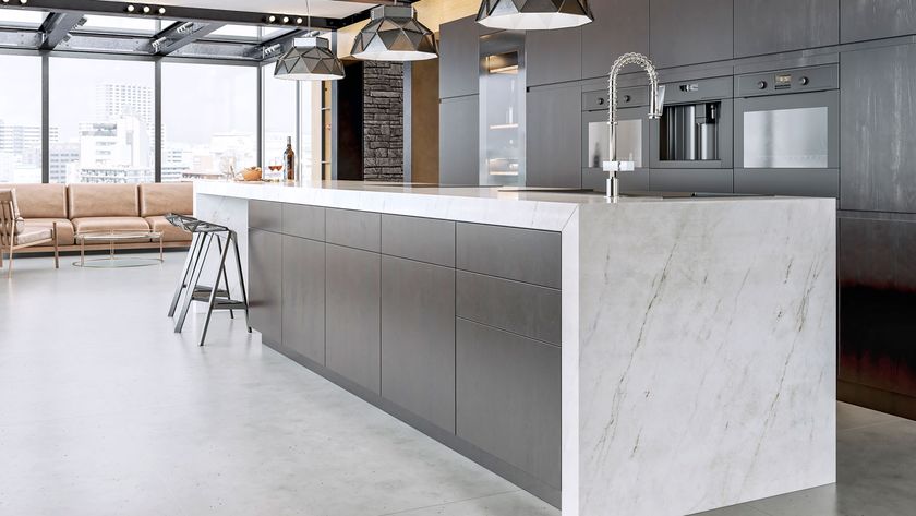 Contemporary apartment with large marble worktop and island with a bank of dark kitchen units in backgound.