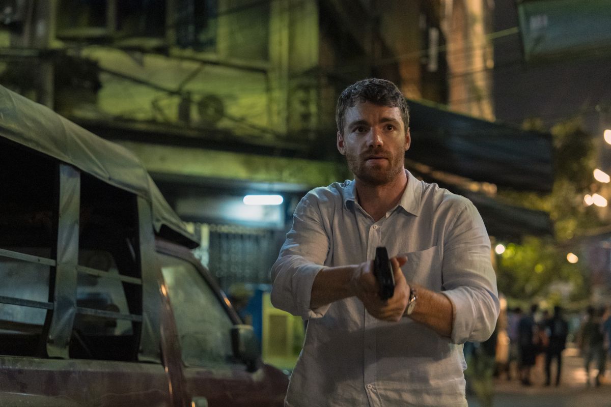 Peter Sutherland holds a gun as he walks through the streets of Thailand in The Night Agent season 2