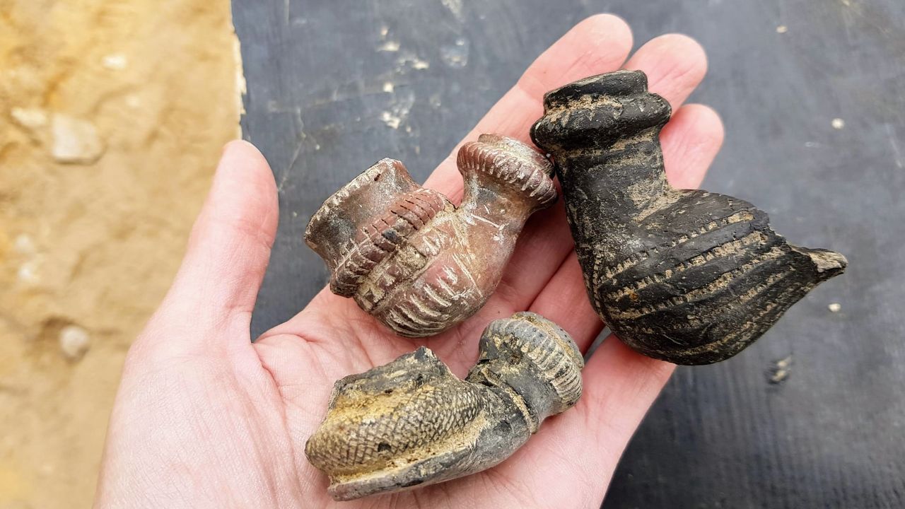 A hand holding 3 small Ottoman-era pipes used for smoking. One is large and black with straight horizontal lines on the body. The other 2 are slightly smaller, one a reddish brown with vertical stipes and the other more gray and covered in dots.