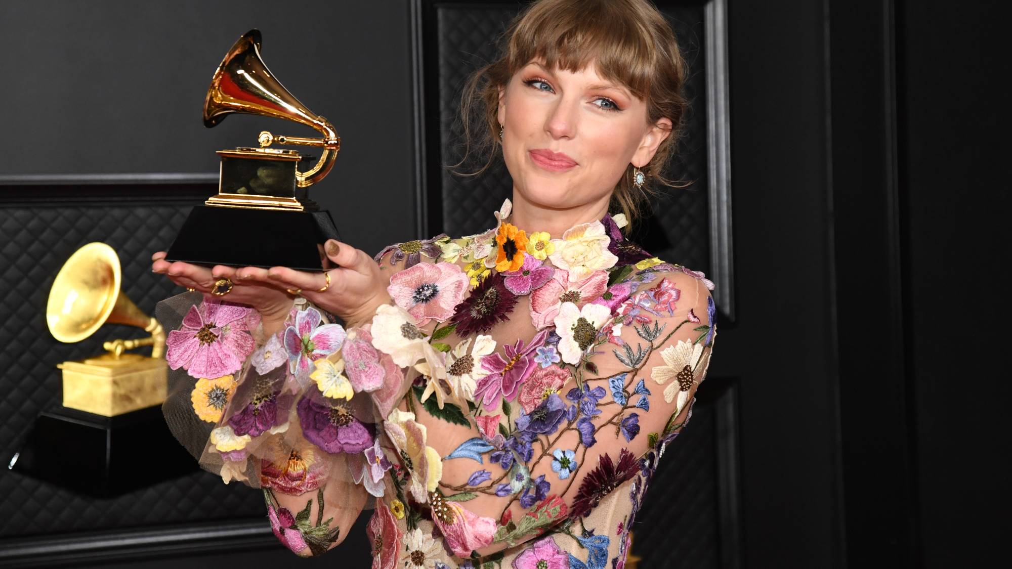 Taylor Swift wears a flower dress and holds up a Grammy award