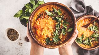 Yellow Indian vegan lentil soup curry with parsley and sesame in a wooden bowl in hands