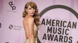 Taylor Swift in gold dress poses in the press room at the American Music Awards