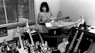 Eddie Van Halen sitting down holding a guitar with lots of other guitars on the floor
