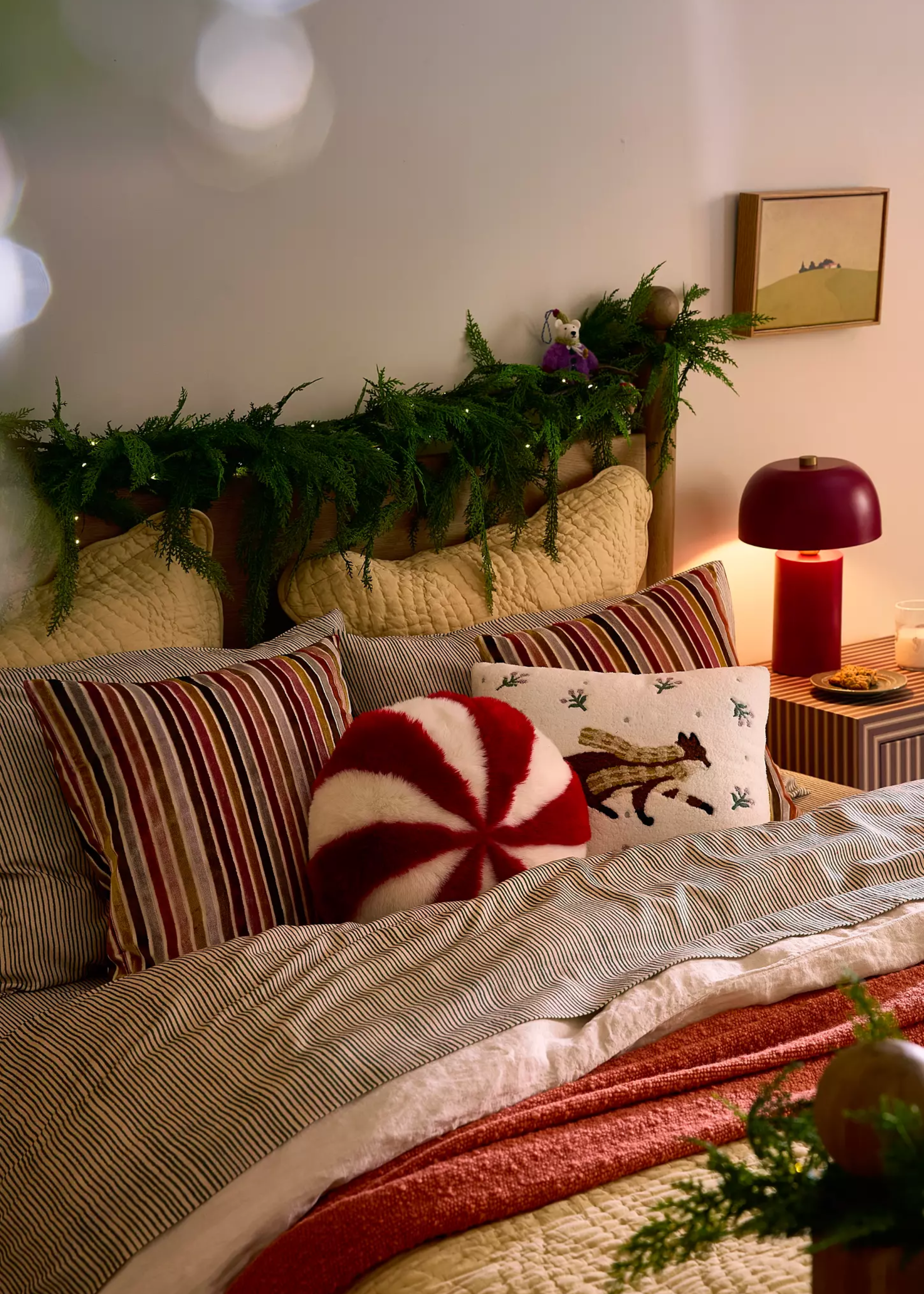 A bed dressed in Christmas bedding and pillows with a garland across the headboard