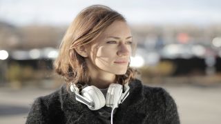 Bästa billiga hörlurar: En kvinna med ett par vita over-ear-hörlurar runt halsen