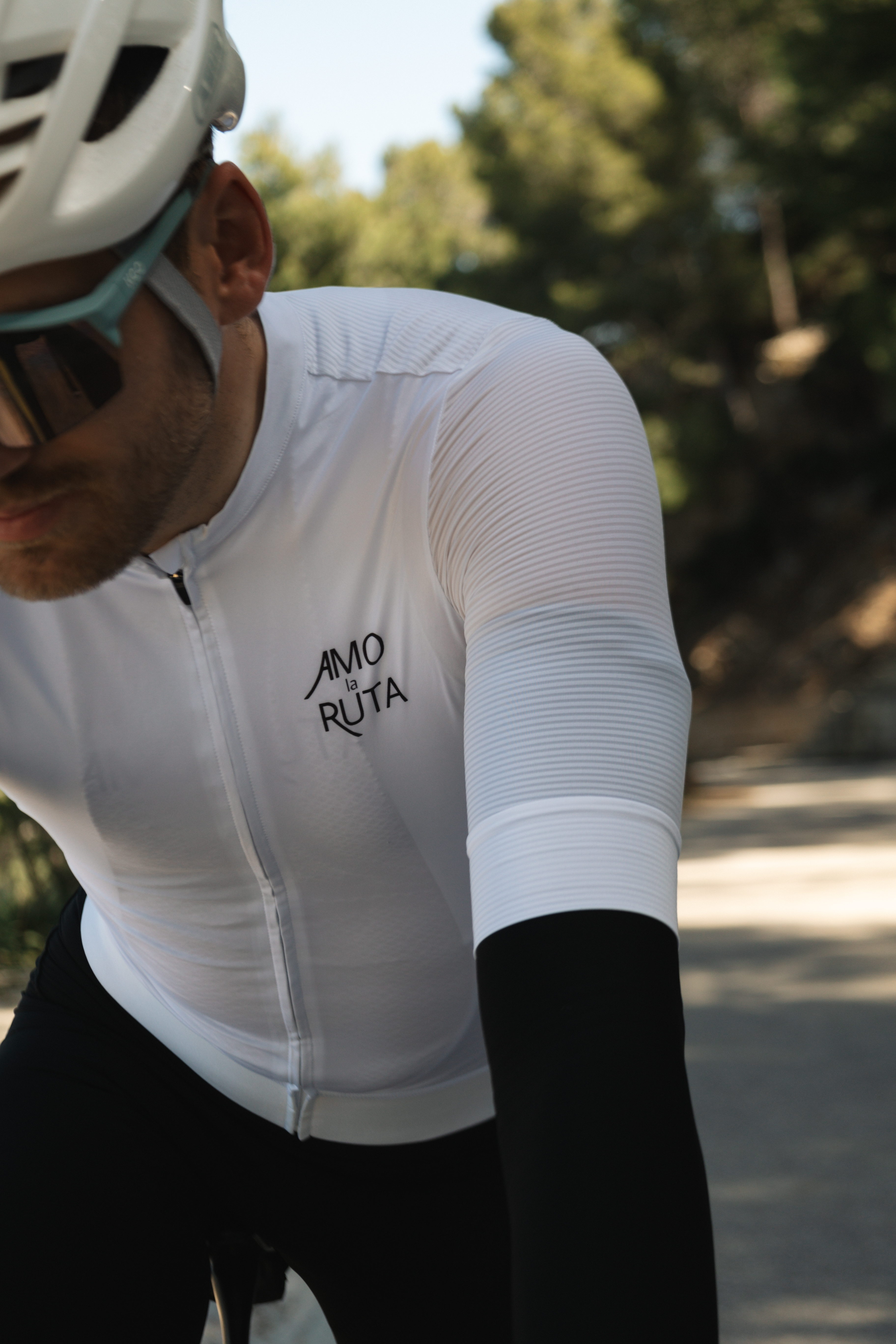 A male cycling wearing a white Amo La Ruta top
