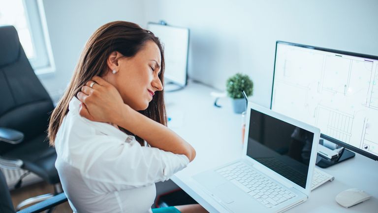 Women strains her neck as she appears to be in pain at her computer desk