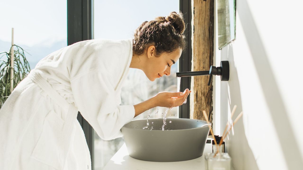 a woman washing her face at a sink