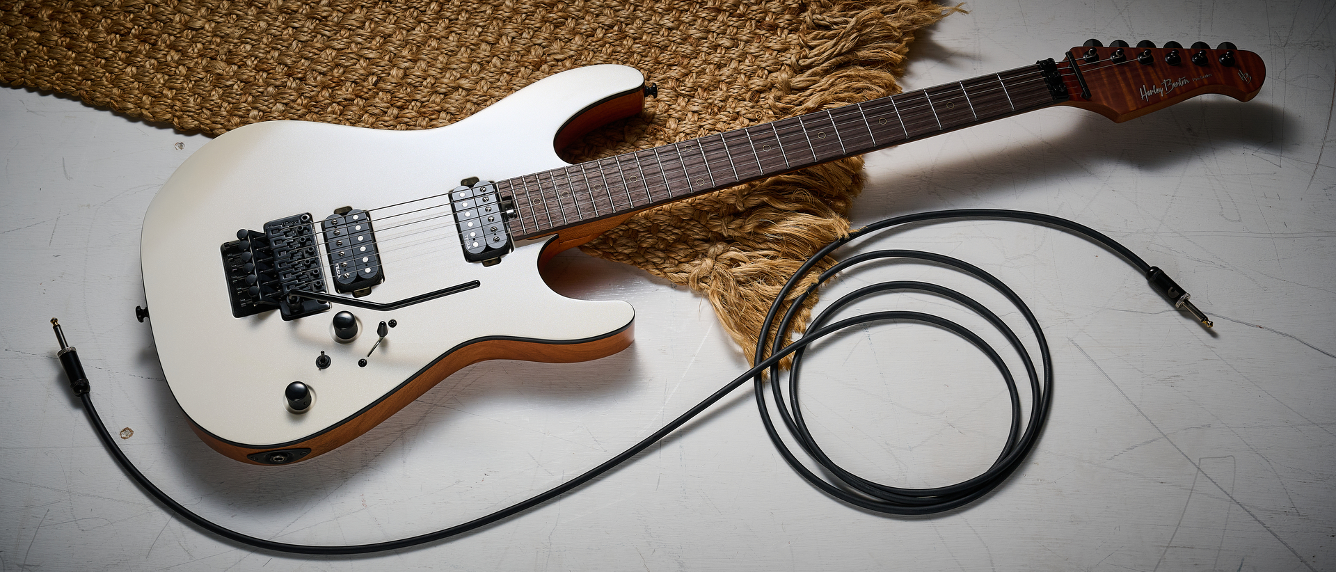 A Harley Benton Fusion IV HH electric guitar on a white floor with a rug and a guitar cable nearby