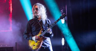 Mikael Åkerfeldt plays his PRS Custom 24 onstage with Opeth in 2023. He wears corpsepaint under the eyes and stands in front of two shafts of bright blue stage lights.