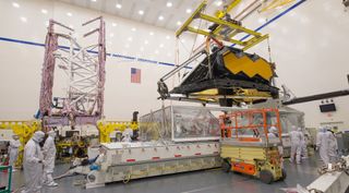 The optical element of NASA's James Webb Space Telescope is removed from a shipping container in a Northrup Grumman clean room in March. The spacecraft element, including the folded-up sunshield, is at left prior to undergoing acoustic testing.