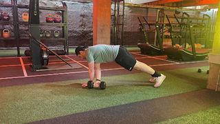 Personal trainer at Gymbox Aaron Cook performing a plank dumbbell through