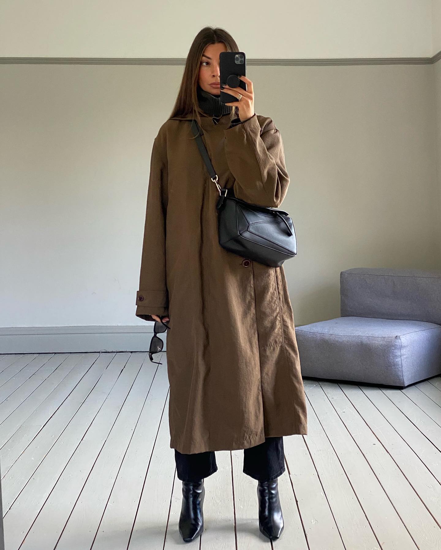 An image of @smythsisters wearing a black Loewe Puzzle bag alongside a beige trench coat, black trousers and black heeled boots.