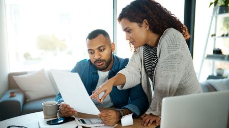 A couple look at paperwork together while working on their finances at the dining room table.