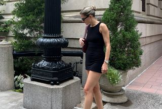 Eliza Huber wearing a black Norma Kamali minidress with black satin mules, sunglasses, and a burgundy Bottega Veneta shoulder bag.