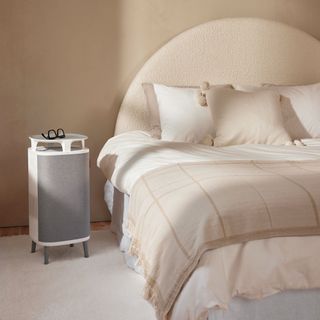 An air purifier with legs by the side of a bed in a peach coloured bedroom