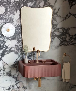 Pink fluted bathroom basin with a gold tap and a gold-framed mirror above it