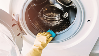 Rubber gloved hand wiping a washing machine rubber with a blue sponge