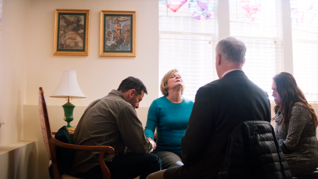 A still of the cast of Mass sat around a table 