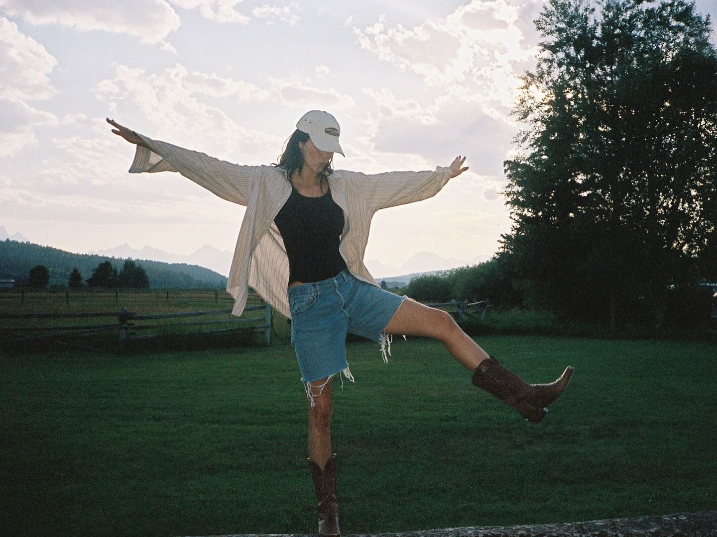 Kendall wears a beige button-down shirt, black tank, frayed-hem bermuda denim shorts and brown cowboy boots.