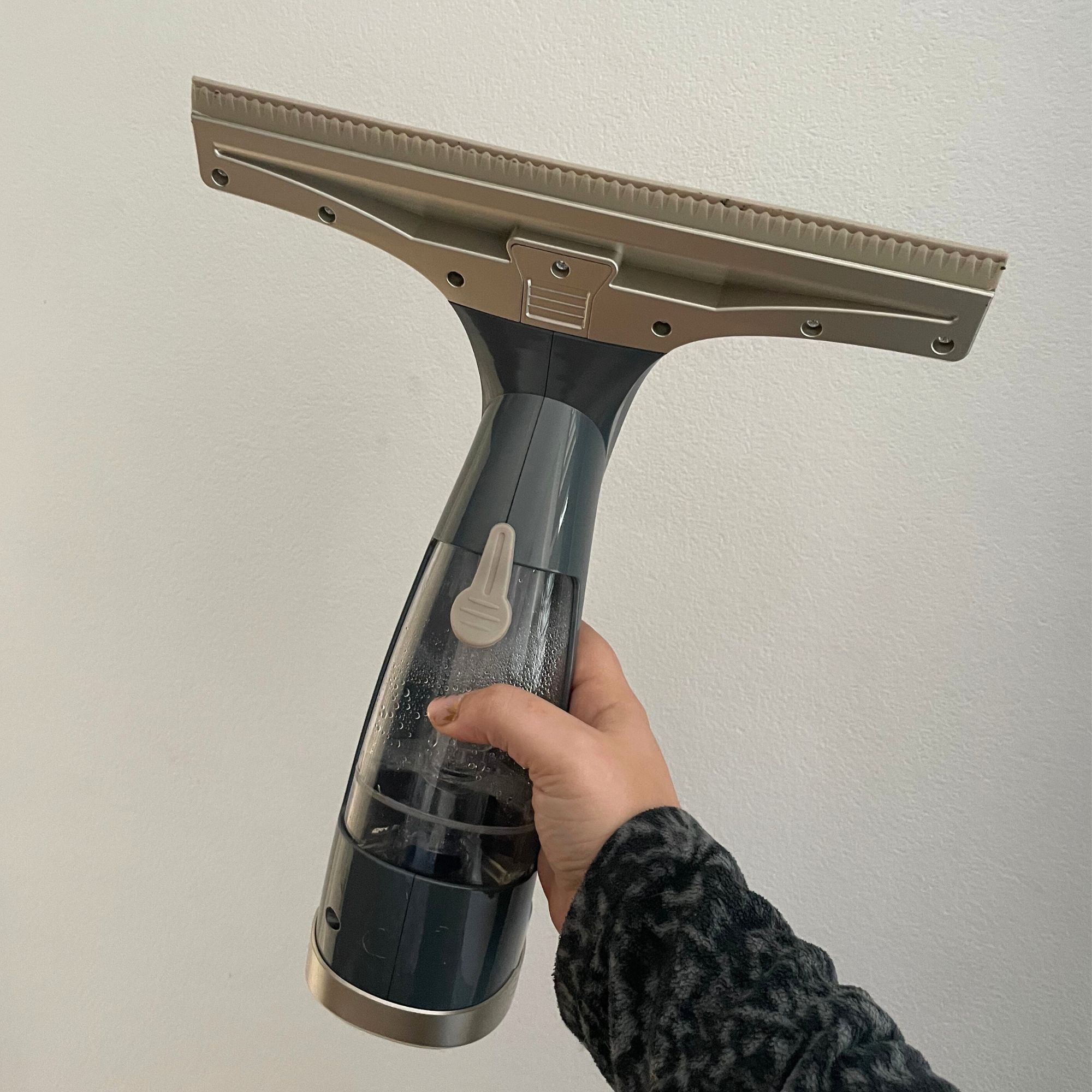 Hand holding a Beldray window vacuum against a white wall