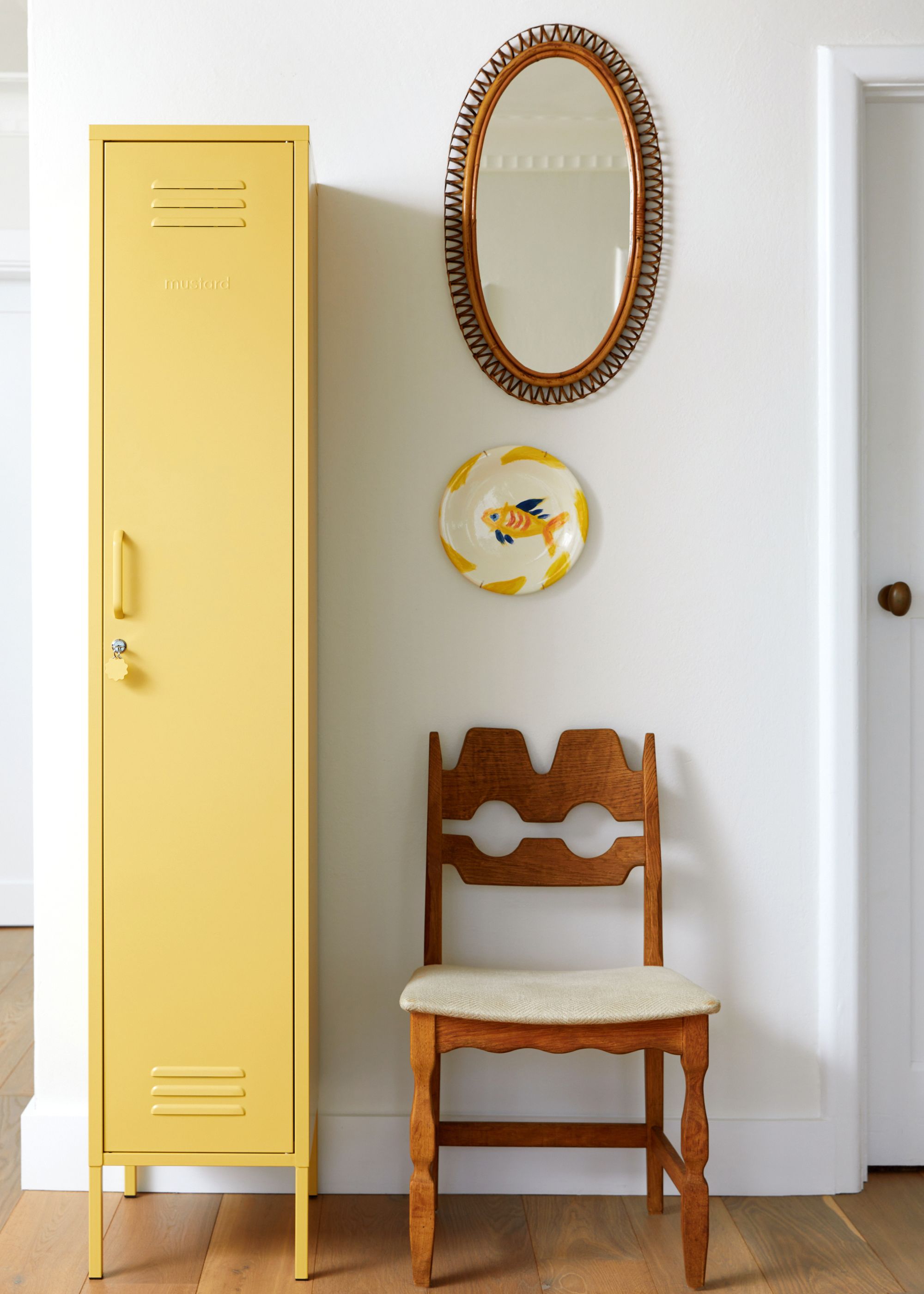 entryway with white wall, wooden chair, and mirror above with butter yellow tall locker unit