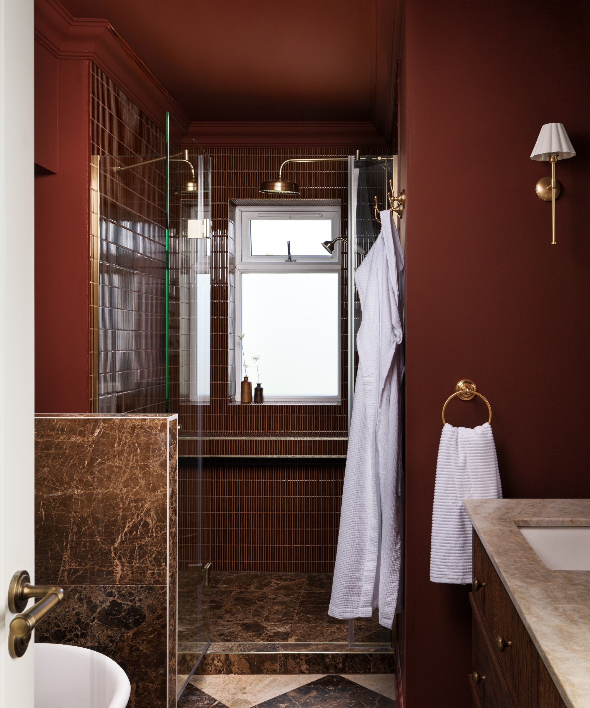 A small shower toom with burgundy shower tiles and brass fixtures