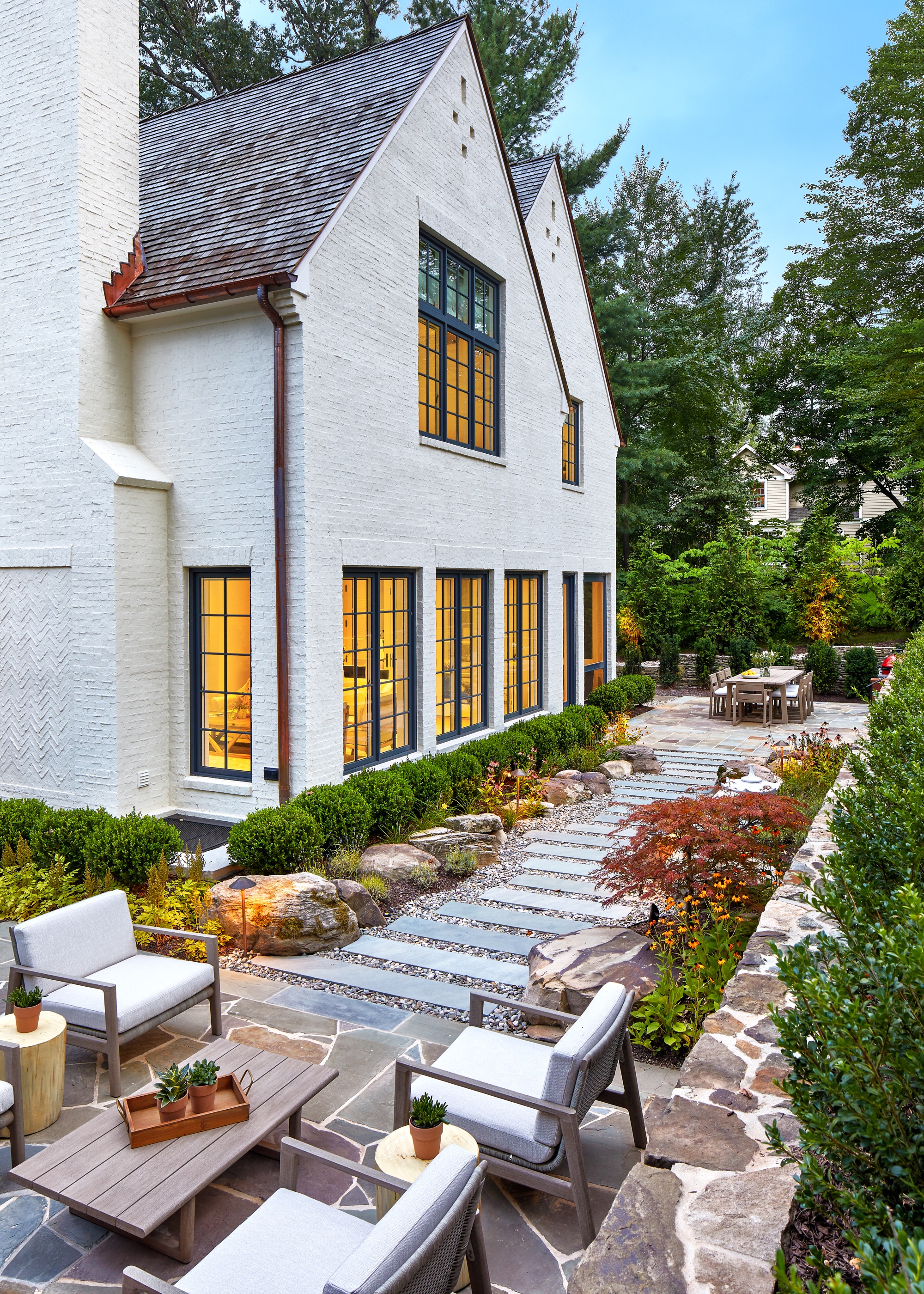 outdoor dining and outdoor living room connected by transitional path that has plants and flowers by the pathways borders