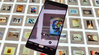 Google Pixel 7 Pro ligger på et lysbord med kamera-app'en åben og mange små og bagbelyste billeder på bordpladen