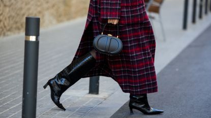 Miss Dior Perfume Cyber Monday: A woman wearing a checkered coat, black leather boots and a black Dior handbag