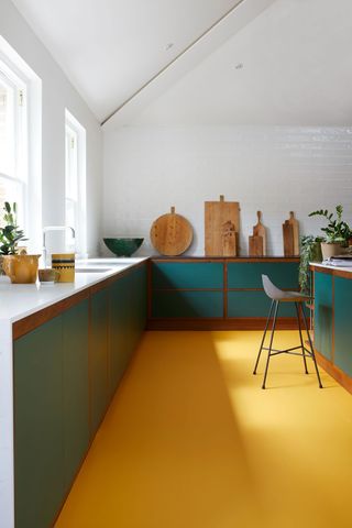 Kitchen with teal green kitchen cabinets with bright yellow floor and wooden chopping boards