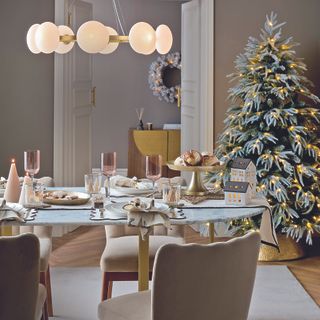 Dining room table with metallic ornaments and candles on top, with a pendant light overhead and a soft white rug underneath